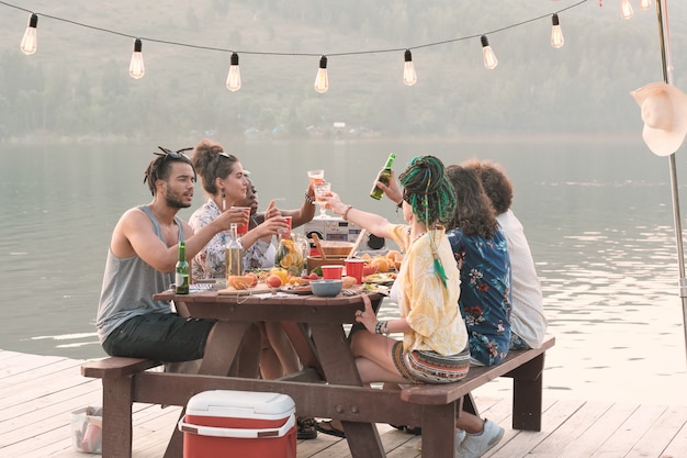 Groep jonge mensen aan de tafel zitten en samen lunchen op een pier buiten