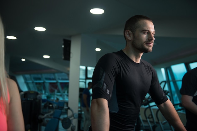 Groep jonge mensen die op loopbanden in de sportschool of fitnessclub lopen terwijl de persoonlijke trainer de tijd meet op de stopwatch