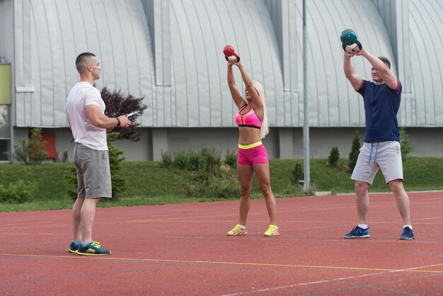 Groep jonge mensen doen een waterkoker Bell-oefening buiten met instructeur