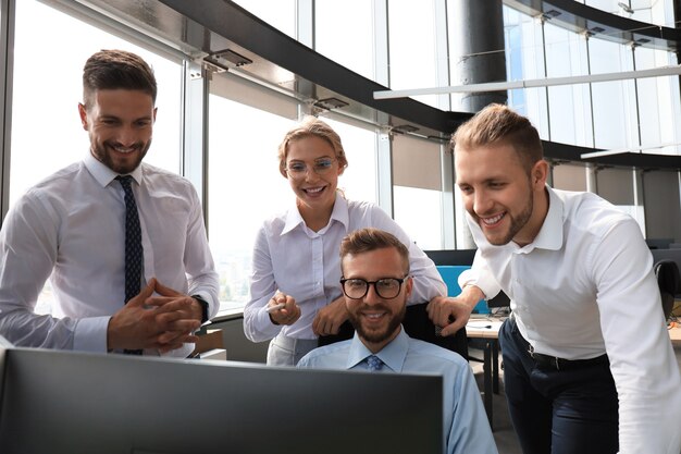 Groep jonge moderne mensen in formalwear die moderne technologieën gebruikt terwijl ze in het creatieve kantoor werken.