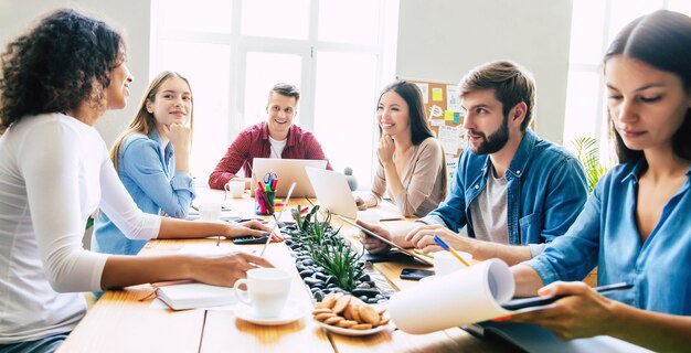 Groep jonge moderne teams in slimme vrijetijdskleding bespreken iets terwijl ze in het creatieve kantoor werken. Beginnen. Coworking ruimte. Ondernemingsideeën