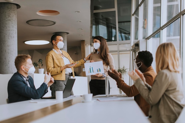 Groep jonge multi-etnische zakenmensen die samenwerken met gezichtsbeschermende maskers en een nieuw project voorbereiden op een vergadering op kantoor