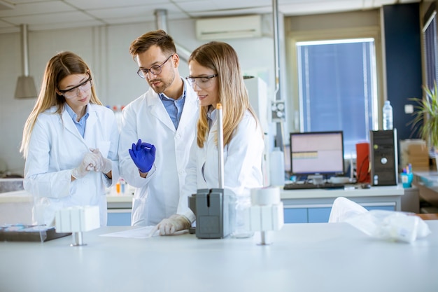 Groep jonge onderzoekers in beschermende werkkleding staan in het laboratorium en analyseren van vloeistofmonsters op ionchromatografie-apparatuur