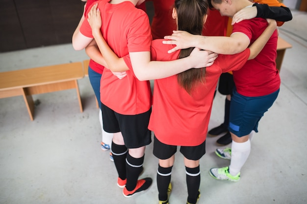 Groep jonge sportieve vrouwen in sportkleding die zich in cirkel bevinden, en vóór spel in kleedkamer bidden