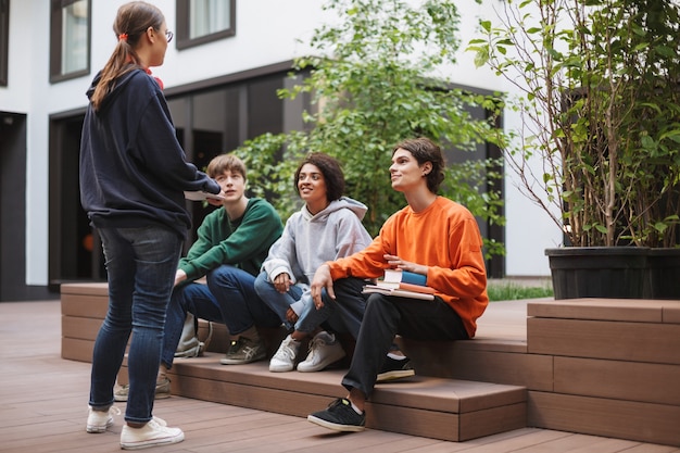 Groep jonge studenten zitten en voorbereiden op les terwijl ze samen studeren op de binnenplaats van de universiteit