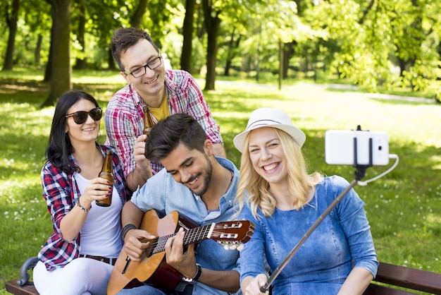 Groep jonge vrienden die gitaar spelen en een selfie nemen op een parkbank