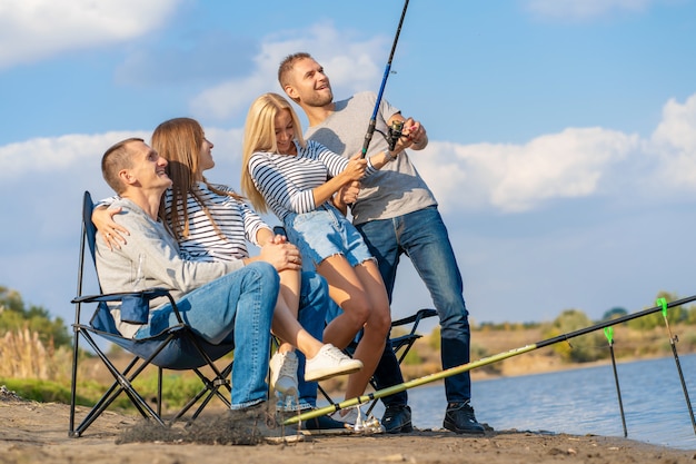 Groep jonge vrienden die op de pijler door oever van het meer vissen