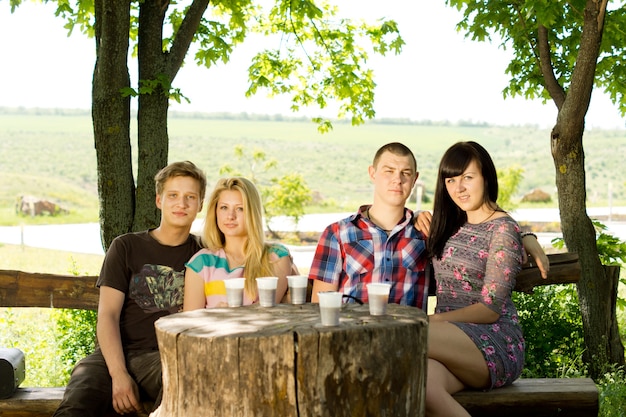 Groep jonge vrienden genieten van een drankje terwijl ze buiten zitten op een rustieke houten bank rond een boomstronktafel