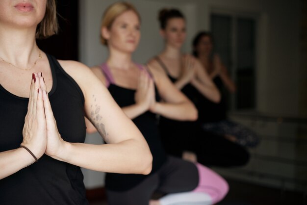 Groep jonge vrouwen die handen in namaste mudra houden wanneer ze samen mediteren in yogastudio