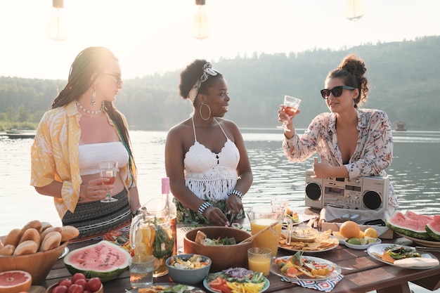 Groep jonge vrouwen die wijn drinken en voedsel bereiden voor het diner op de natuur buitenshuis