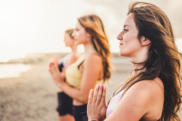 Groep jonge vrouwen, mooie gezonde vrienden in yoga-meditatie buiten op het strand voor een actief wellnessconcept - sport en mensen