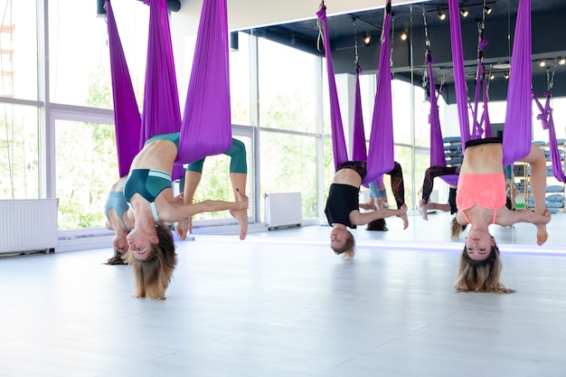 Groep jonge vrouwen oefenen in aero stretching swing. Lucht vliegende yoga-oefeningen oefenen in paarse hangmat in fitnessclub.