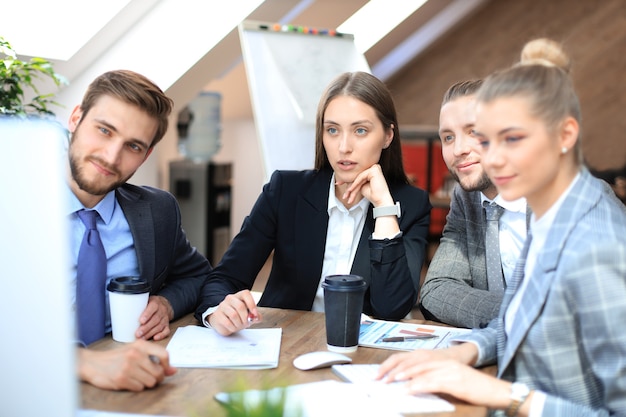 Groep jonge zakenmensen die werken, communiceren terwijl ze samen met collega's aan het bureau zitten.