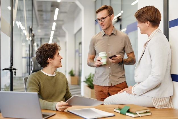 Groep jongeren chatten met nieuwe werknemer op werkplek in moderne kantoorruimte