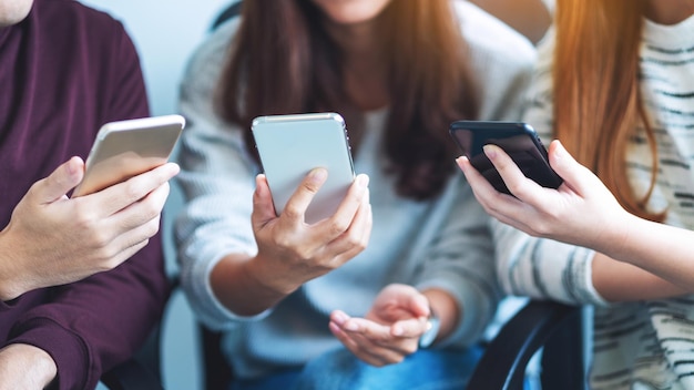 Groep jongeren die mobiele telefoon gebruiken en bekijken terwijl ze samen zitten