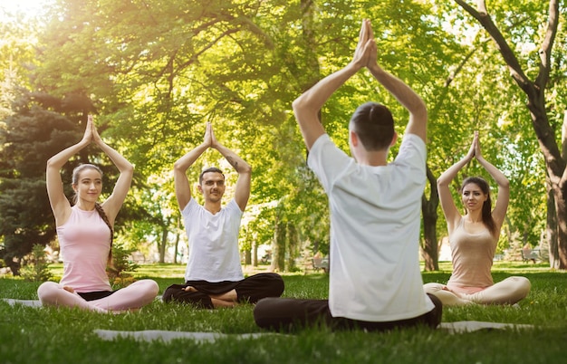 Groep jongeren die yoga beoefenen met coach in park, ademhalingsoefening maken met instructeur, ruimte kopiëren