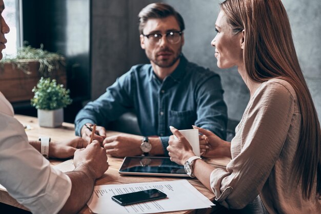 Groep jongeren in slimme vrijetijdskleding die iets bespreken terwijl ze samen op kantoor werken