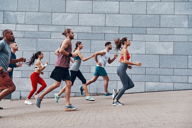 Groep jongeren in sportkleding joggen tijdens het sporten op het trottoir buitenshuis