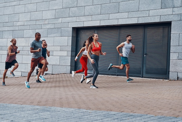 Groep jongeren in sportkleding joggen tijdens het sporten op het trottoir buitenshuis