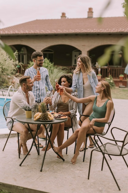 Groep jongeren juichen met cider bij het zwembad in de tuin