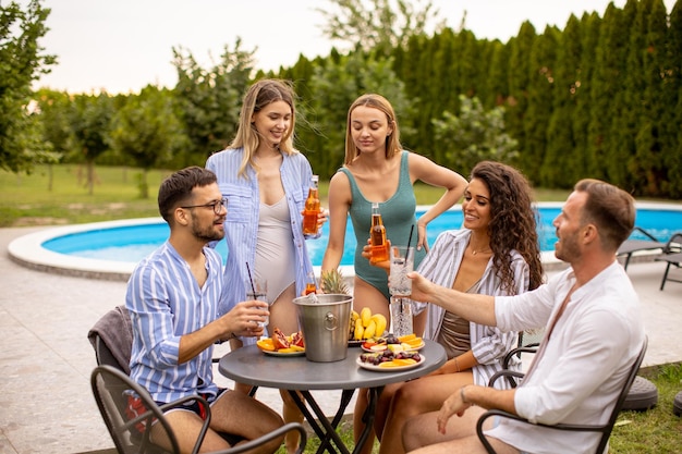 Groep jongeren juichen met cider bij het zwembad in de tuin