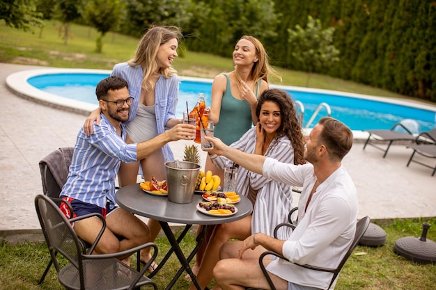 Groep jongeren juichen met cider bij het zwembad in de tuin