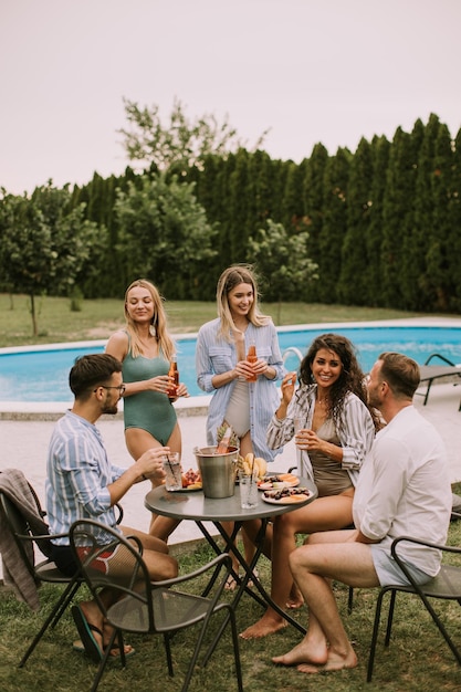 Groep jongeren juichen met cider bij het zwembad in de tuin