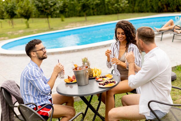 Groep jongeren juichen met drankjes en eten fruit bij het zwembad in de tuin
