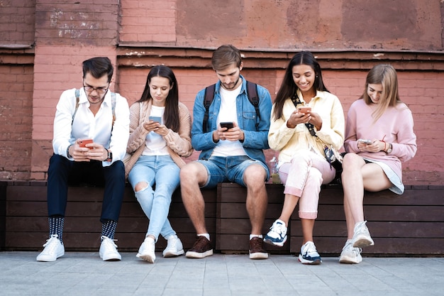 Groep jongeren met behulp van gadgets buiten zitten