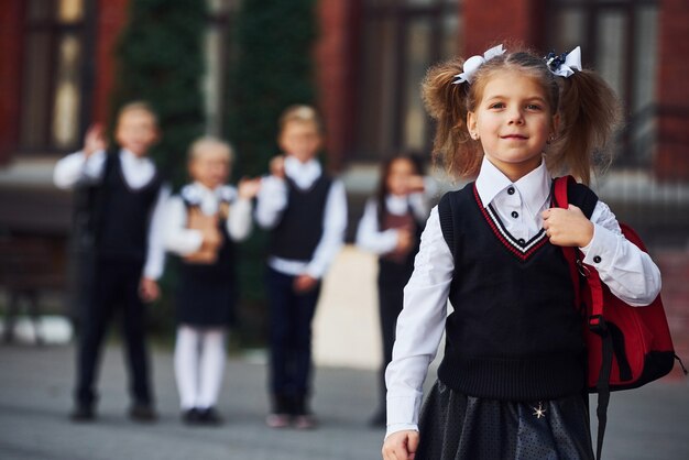 Groep kinderen in schooluniform poseren voor de camera buiten samen in de buurt van onderwijsgebouw.