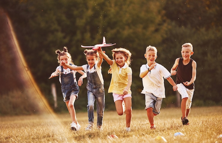 Foto groep kinderen plezier buitenshuis met rood speelgoed vliegtuig in handen.