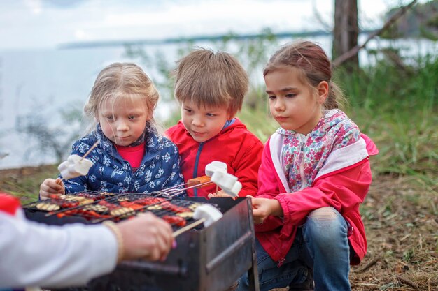 Groep kinderen zitten bij het vuur en bereiden zich voor om marshmallow-snoepjes op kampvuur te bakken, wandelen in het weekend, lokaal reizen na lockdown, staycation