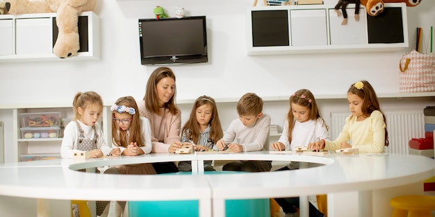 Groep kleine kinderen spelen met voorschoolse houten educatief speelgoed met kleuterjuf