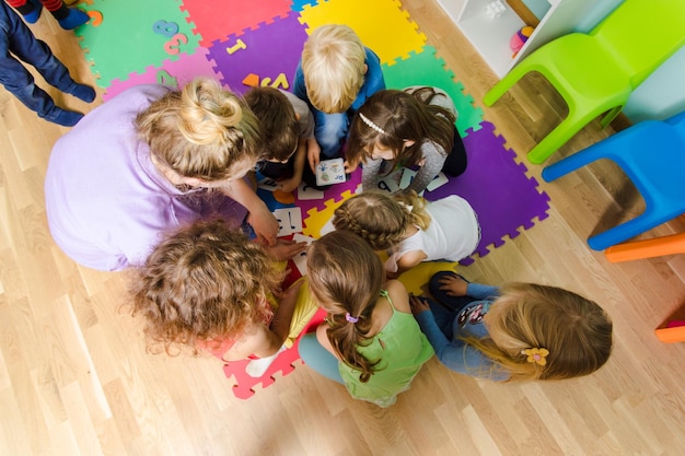 Groep kleuters die dicht op een vloer zitten samen met een leraar die groepswerk geeft Kinderen leren samenwerken tijdens het oplossen van taken