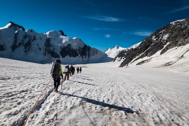 Groep klimmers met rugzakken wordt aan elkaar vastgebonden en stijgt op gletsjer in besneeuwde bergen