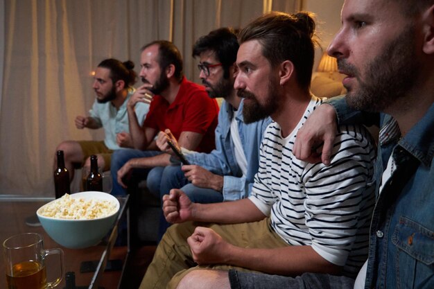 Groep mannen geconcentreerd op de bank in een woonkamer die naar een voetbalwedstrijd kijken