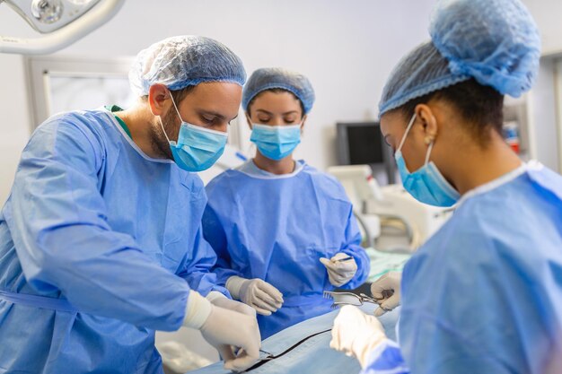 Groep medisch team die dringend een chirurgische ingreep uitvoert en de patiënt helpt in het theater in het ziekenhuis Medisch team dat een chirurgische ingreep uitvoert in een lichte moderne operatiekamer