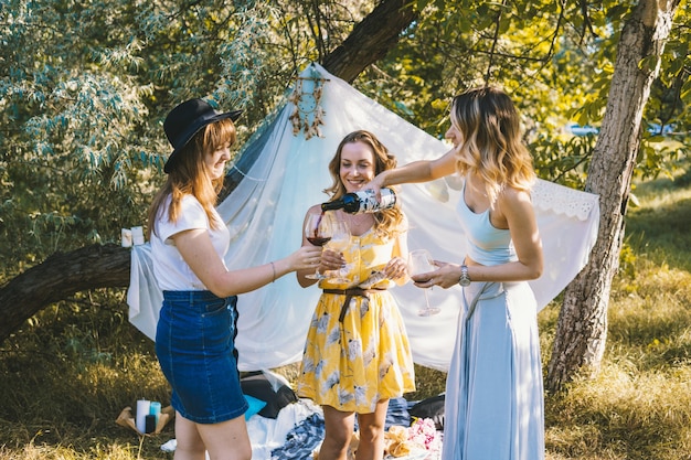 Groep meisjesvrienden die picknick buiten maken. Ze schenken wijn uit een fles in glazen.