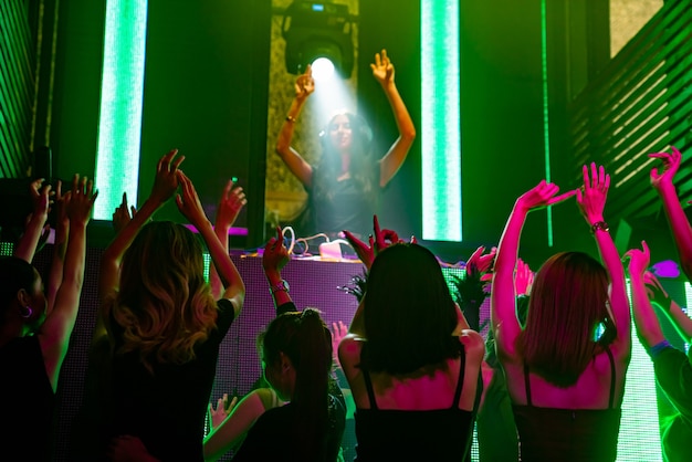 Foto groep mensen dansen in disco nachtclub op het ritme van muziek van dj op het podium
