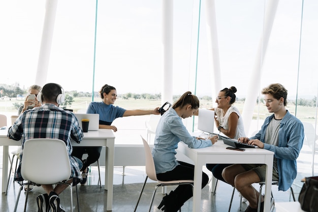 Groep mensen die aan aparte tafels werken in een coworking met laptops, mobiele telefoons en koffie