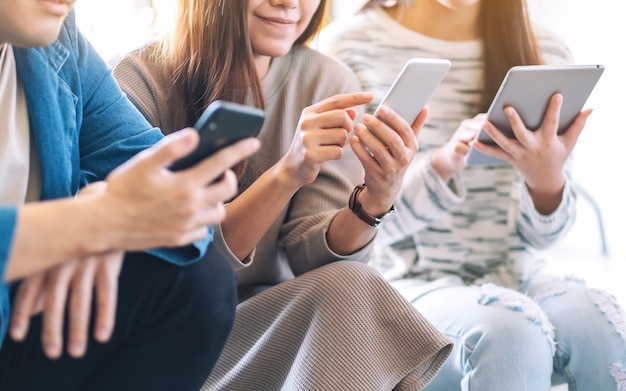 Groep mensen die mobiele telefoon en tablet-pc gebruiken en bekijken terwijl ze samen zitten