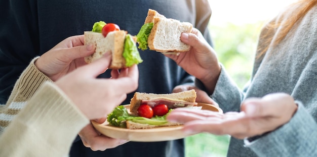 Groep mensen die volkoren sandwich in houten plaat samen houden en eten