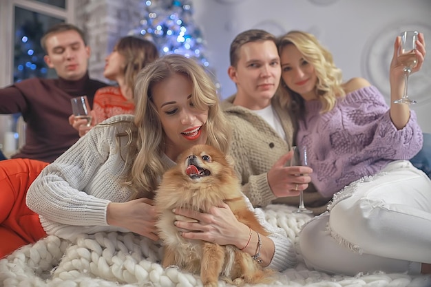 groep mensen en een hond in het nieuwjaarsinterieur / vrienden van jongens en meisjes Kerstavond met champagne