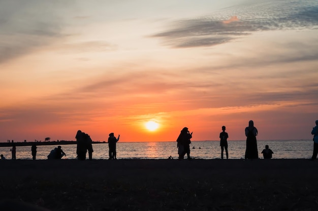 Groep mensen genieten van de zonsondergang op het strand. Zonsondergangachtergrond en silhouetten van mensen