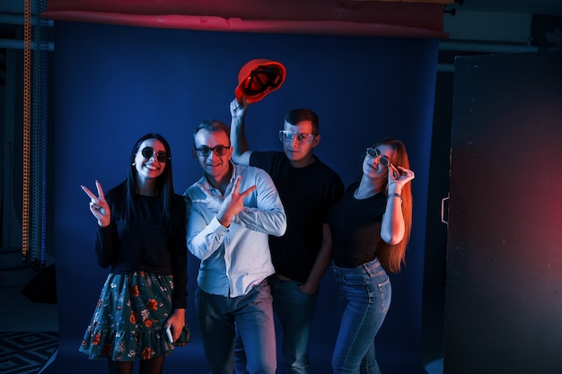 Groep mensen in vrijetijdskleding en glazen staat en veel plezier binnenshuis in de studio met neonverlichting.