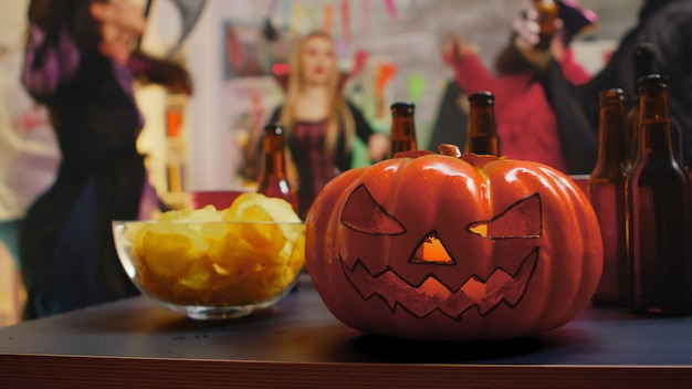 Groep mensen met kostuums die halloween vieren en dansen. Chips en bier voor het feest.