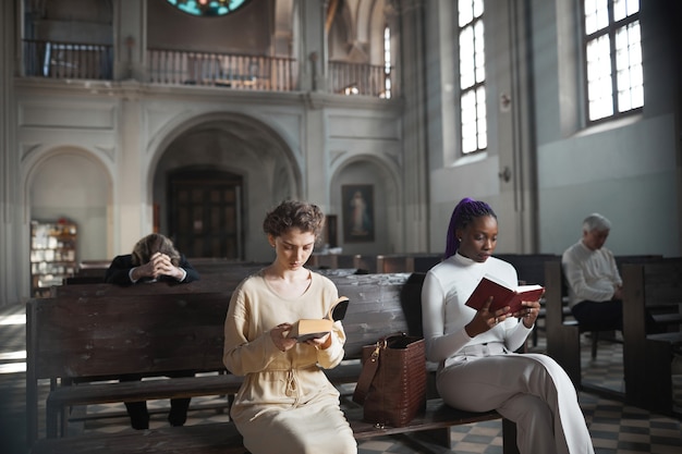 Groep mensen zittend op de bank Bijbel lezen en bidden tijdens de mis in de kerk