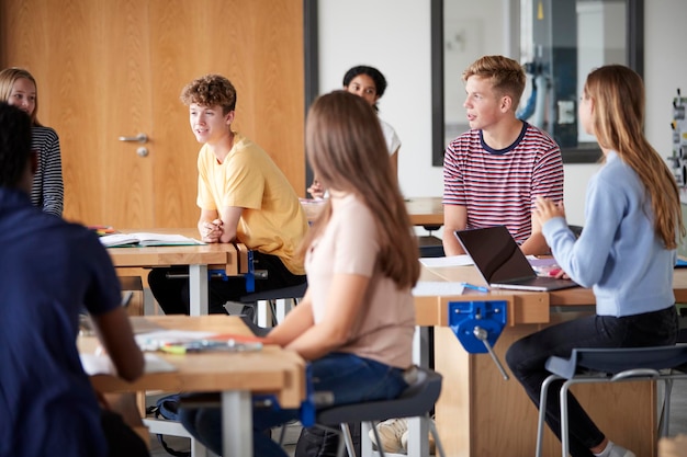 Groep middelbare scholieren die op werkbanken zitten en een discussie hebben in de les over ontwerp en technologie