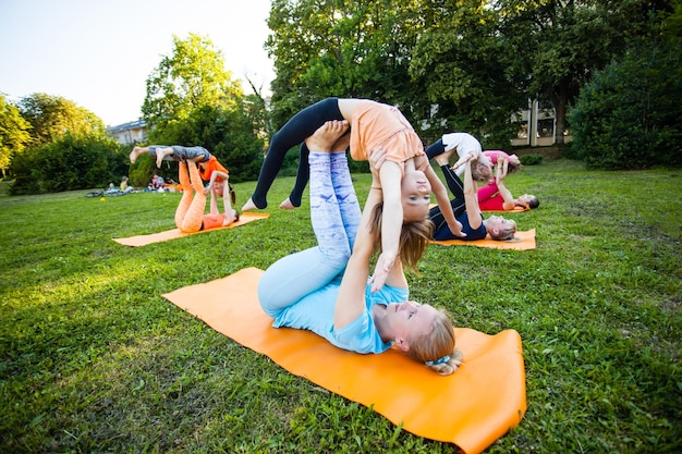 Groep moeders en hun kinderen die oefeningen doen die yoga beoefenen op een fitnesskleed in de frisse lucht
