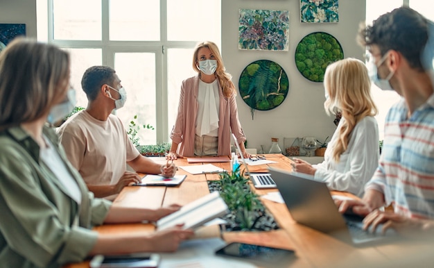 Groep multiraciale mensen die tijdens het coronavirus in een modern kantoor werken. Jonge zakenmensen en senior baas werken samen met gezichtsbeschermende maskers. Preventieve maatregelen tijdens Covid-19